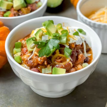 Pumpkin turkey chili in a white bowl on a silver surface and more bowls in the background.