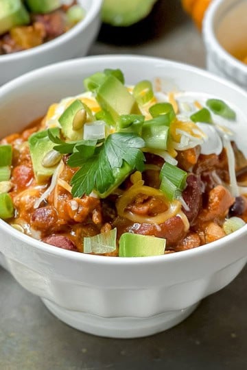 Pumpkin turkey chili in a white bowl on a silver surface and more bowls in the background.