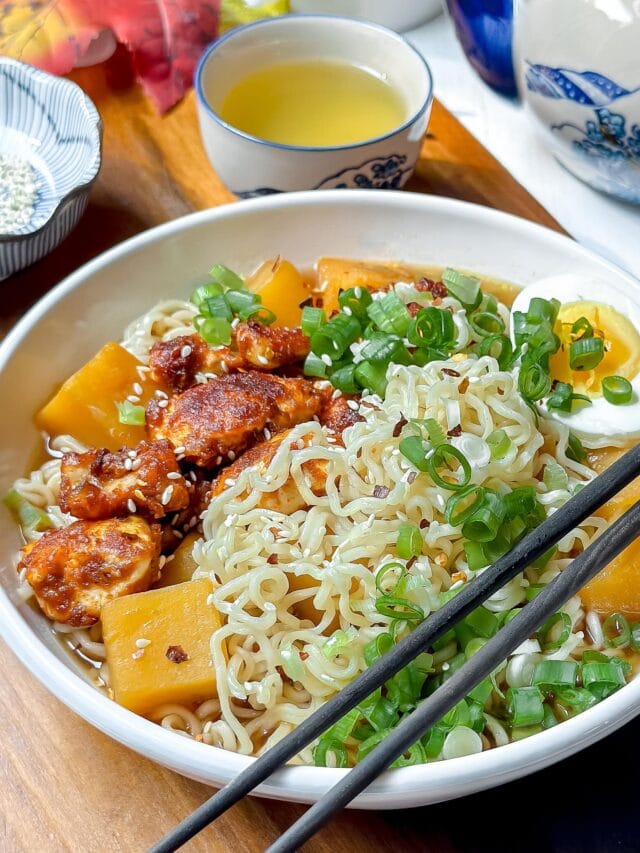 Side view of Curry Chicken Ramen in a white bowl with chopped green onions, chopsticks and seasame seeds.