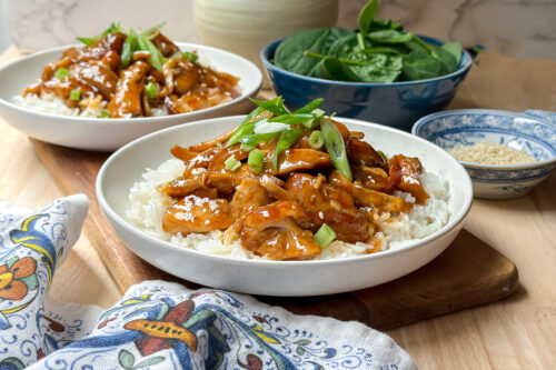 Horizontal view of Crockpot Honey Garlic Chicken with chopped green onions in a white bowl