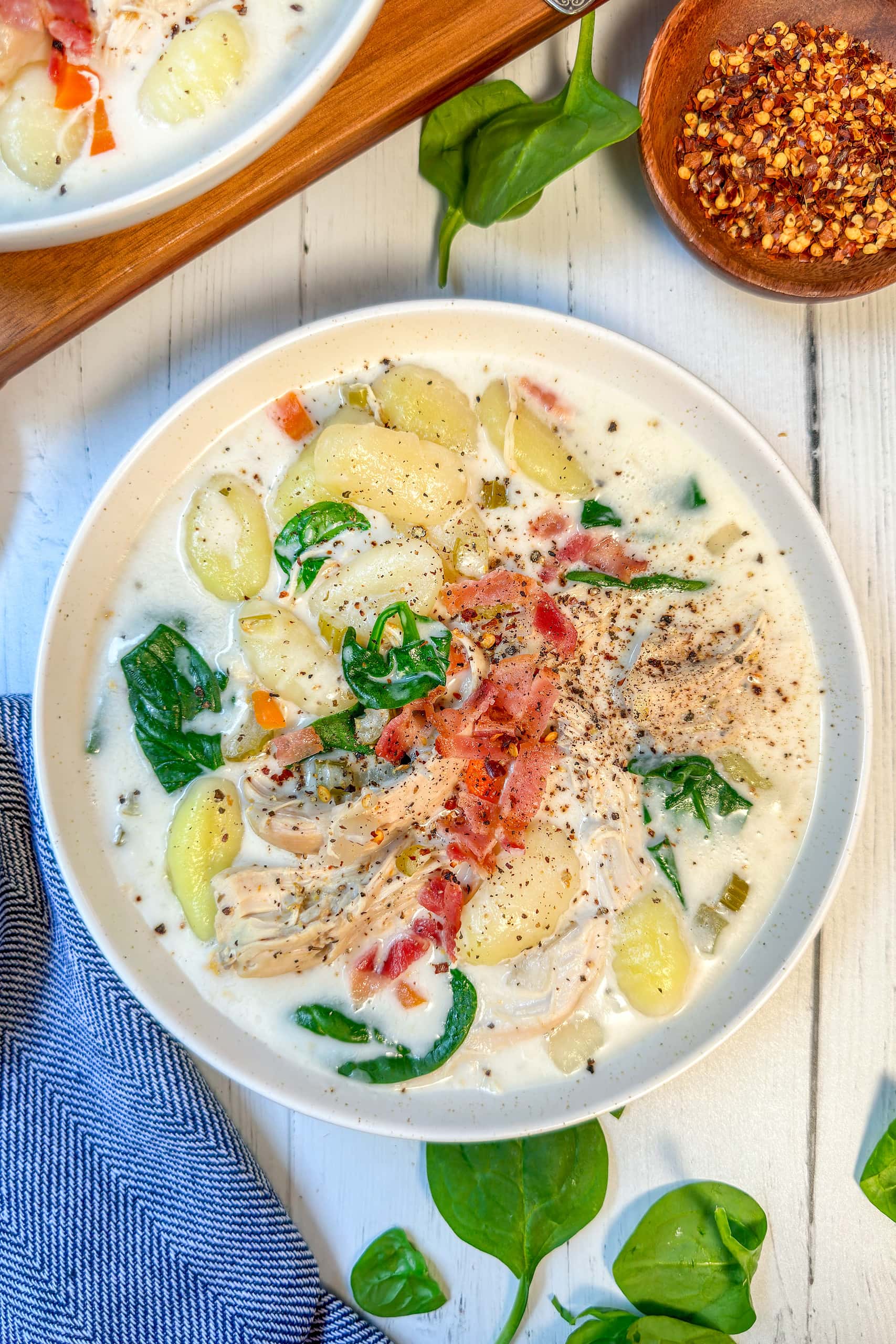 Top view of Crockpot Chicken Gnocchi Soup in spinach and bacon in a white bowl.
