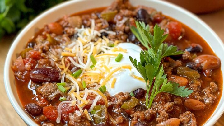 Side view of Crockpot Chili in a blue and white bowl with sour cream, shredded cheese and fresh parsley.