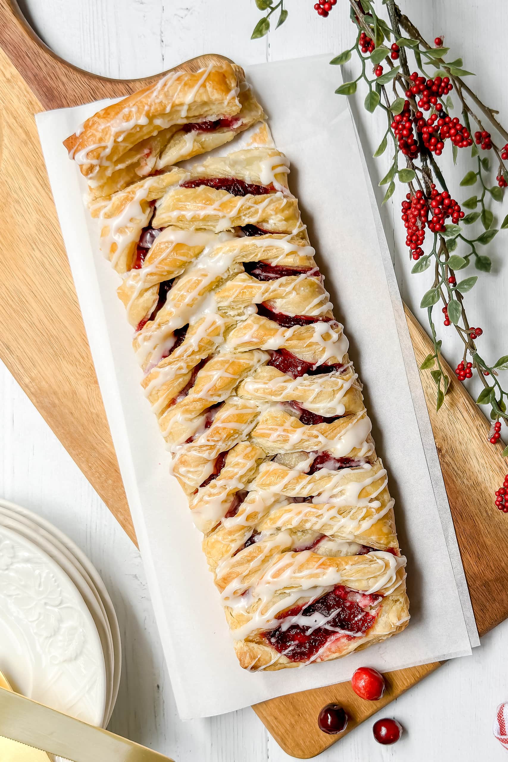 Top view of unsliced and glazed Cranberry Cream Cheese Danish on a wood cutting board.