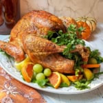 Square image of Self Basting Roast Turkey stuffed with fresh herbs on a serving platter with fresh citrus garnish.