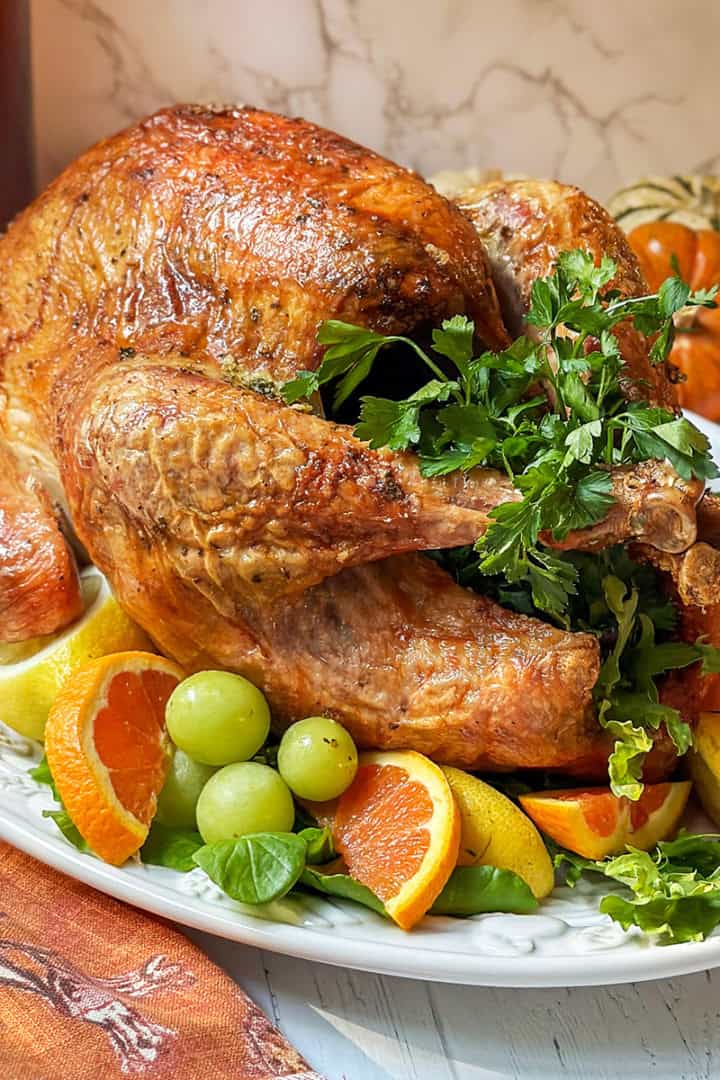 Square image of Self Basting Roast Turkey stuffed with fresh herbs on a serving platter with fresh citrus garnish.