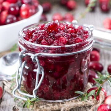 Homemade cranberry sauce in a lidded jar with fresh herbs around the container.