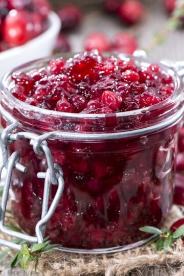 Homemade cranberry sauce in a lidded jar with fresh herbs around the container.