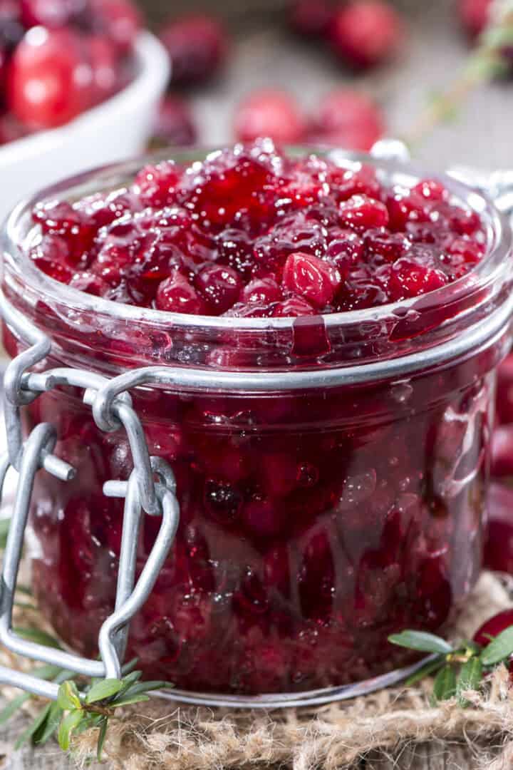 Homemade cranberry sauce in a lidded jar with fresh herbs around the container.