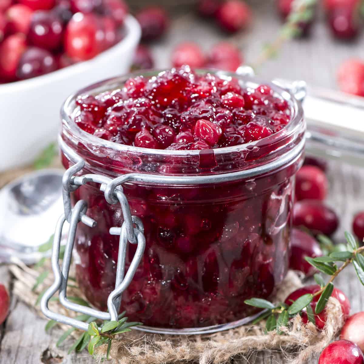 Homemade cranberry sauce in a lidded jar with fresh herbs around the container.