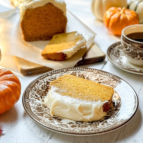 Horizontal closeup view of a slice of pumpkin cracker bread with cream cheese frosting on a brown and white plate