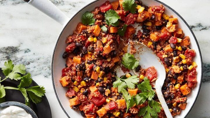 Top view of vegetarian Mexican Skillet Quinoa in a white skillet over a marble background with fresh chopped cilantro on top.
