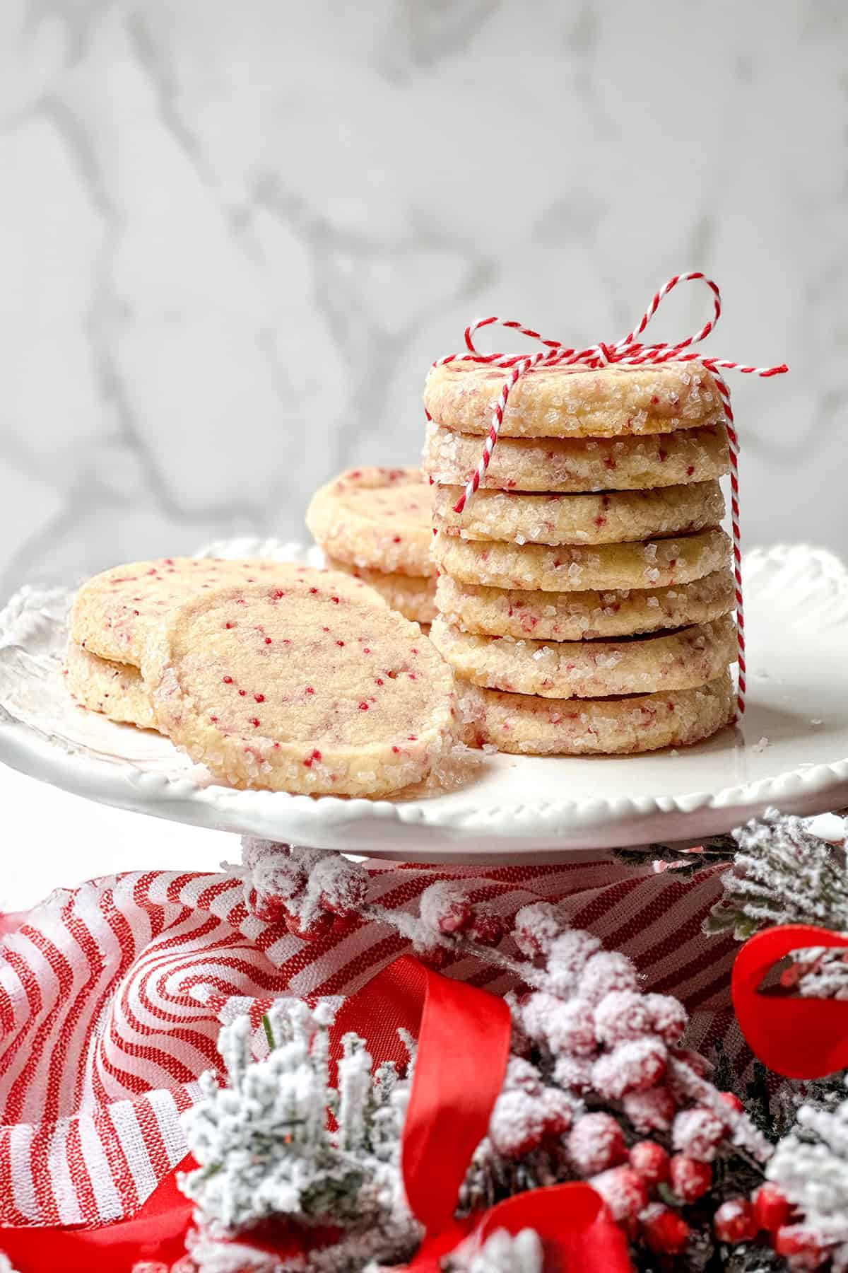 Stack of Christmas slice and bake cookies with more on the side on a white serving platter and tied with a festive ribbon.
