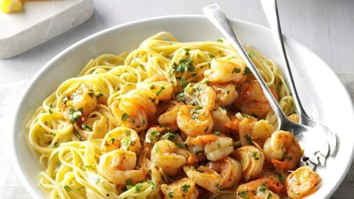 Side view of Garlic Lemon Shrimp served over spaghetti in a white bowl with 2 silver utensils.