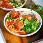 Square image of crockpot turkey meatballs and spaghetti in a white bowl garnished with fresh parsley and chopped green onions for serving.