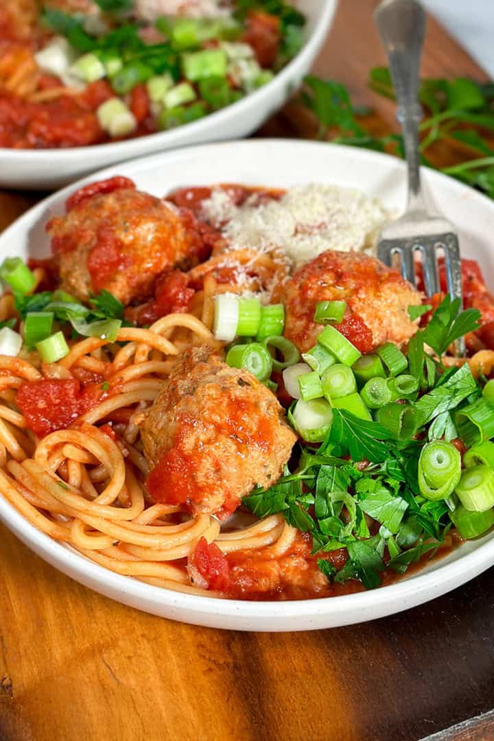Square image of crockpot turkey meatballs and spaghetti in a white bowl garnished with fresh parsley and chopped green onions for serving.