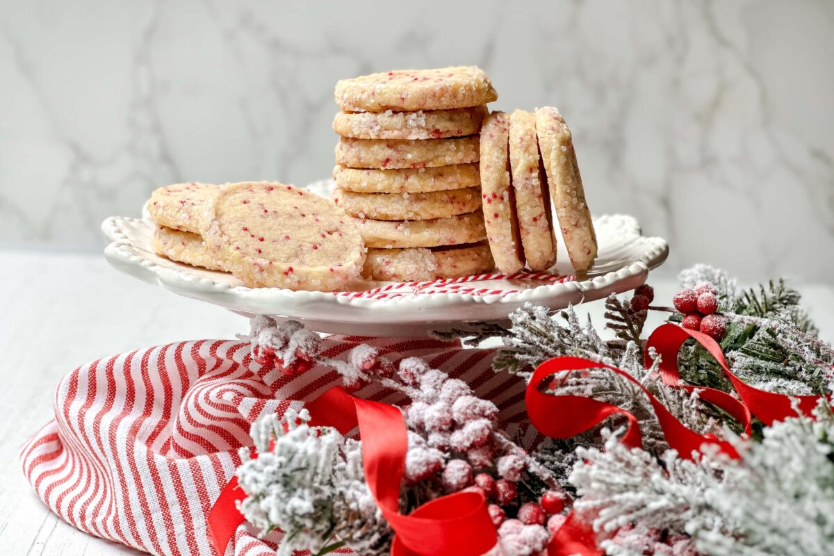 Horizontal side view of stacked Christmas Icebox Cookies with red and white greenery on a white cake plate stand.