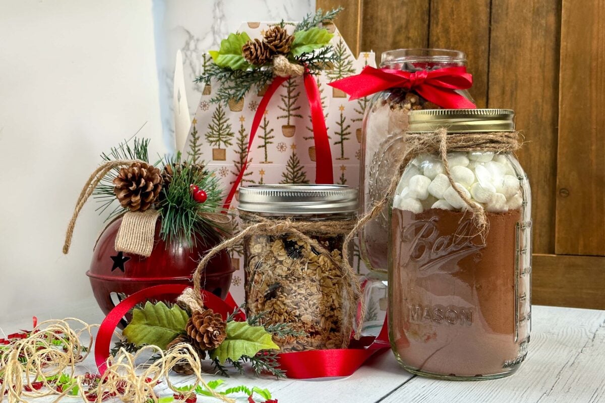 Side horizontal view of festive wrapped Mason Jar Food Gifts in red ribbons and faux greenery.