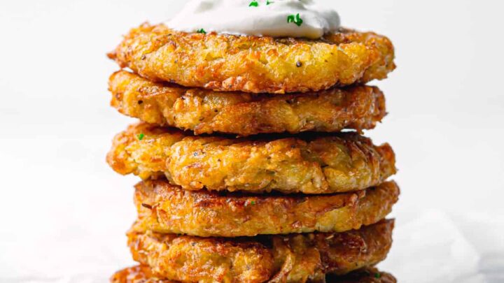 Side view of stacked potato latkes topped with cream and fresh chives.