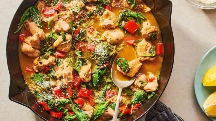 Top view of Skillet Lemon Chicken with spinach in a grey Staub skillet with lemon wedges on the side.