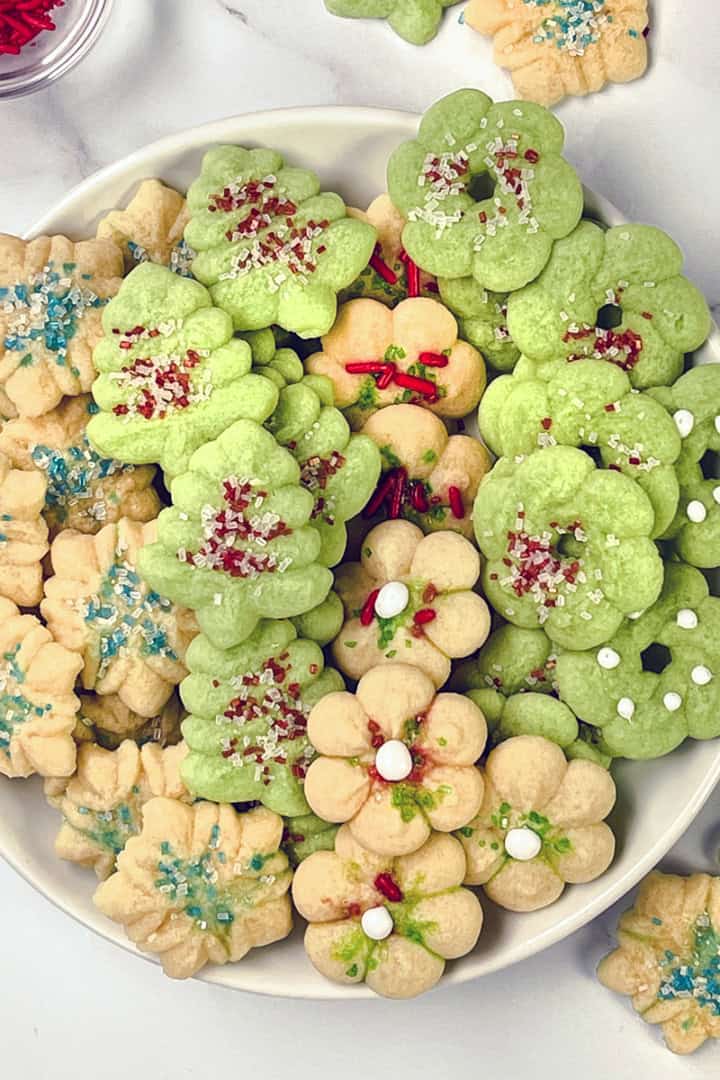 Square image of colorful spritz cookies on a large plate and decorated with sprinkles.