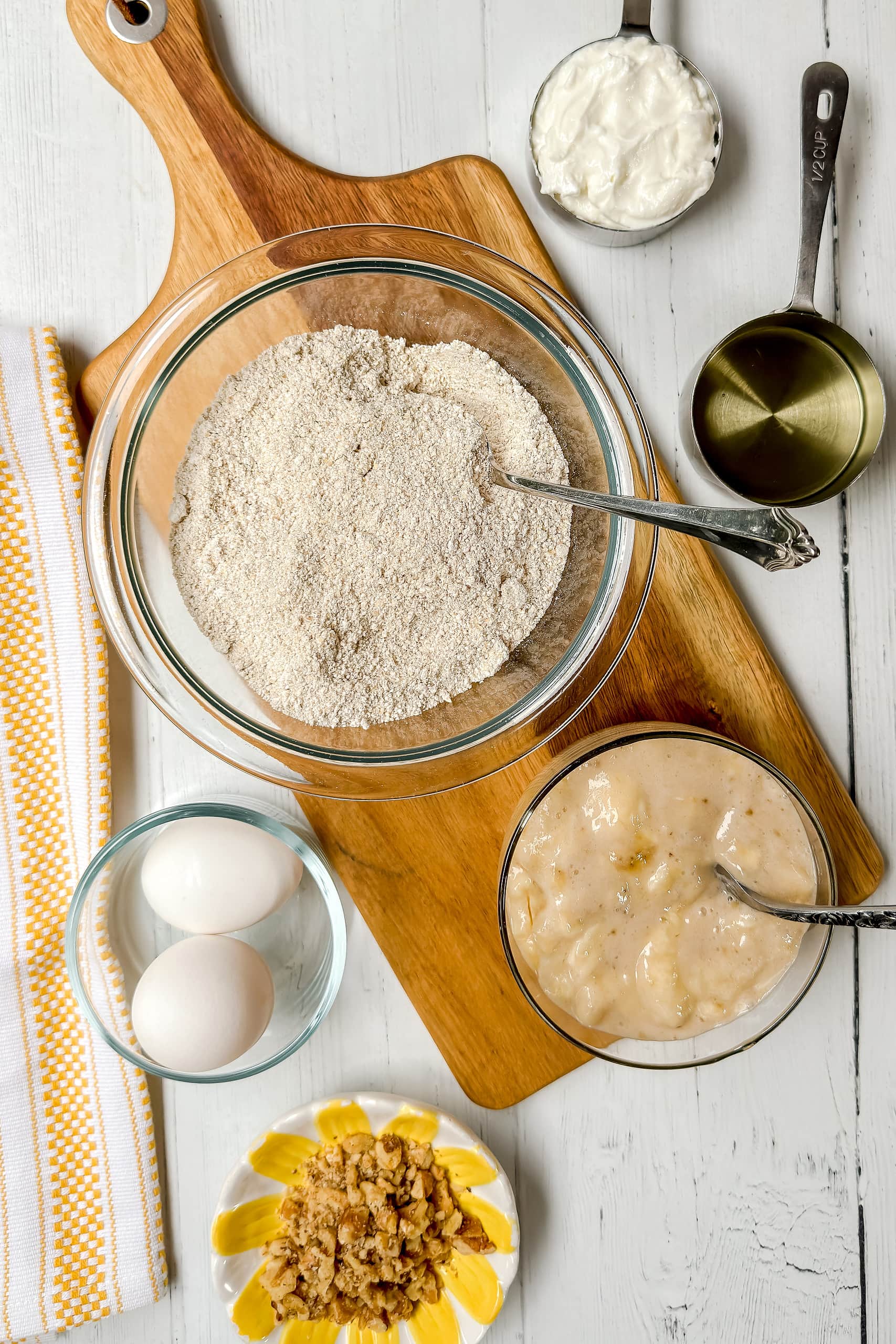 Top view of Oat Flour Banana Bread ingredients on a wood cutting board with a yellow and white kitchen towel.
