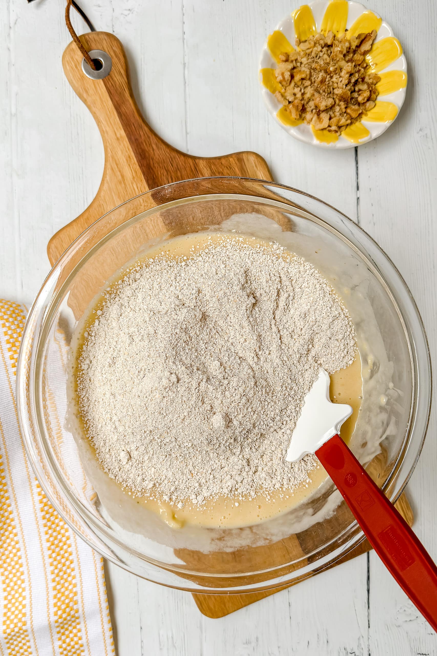 Top view of oat flour being combined into banana bread batter in a glass bowl.