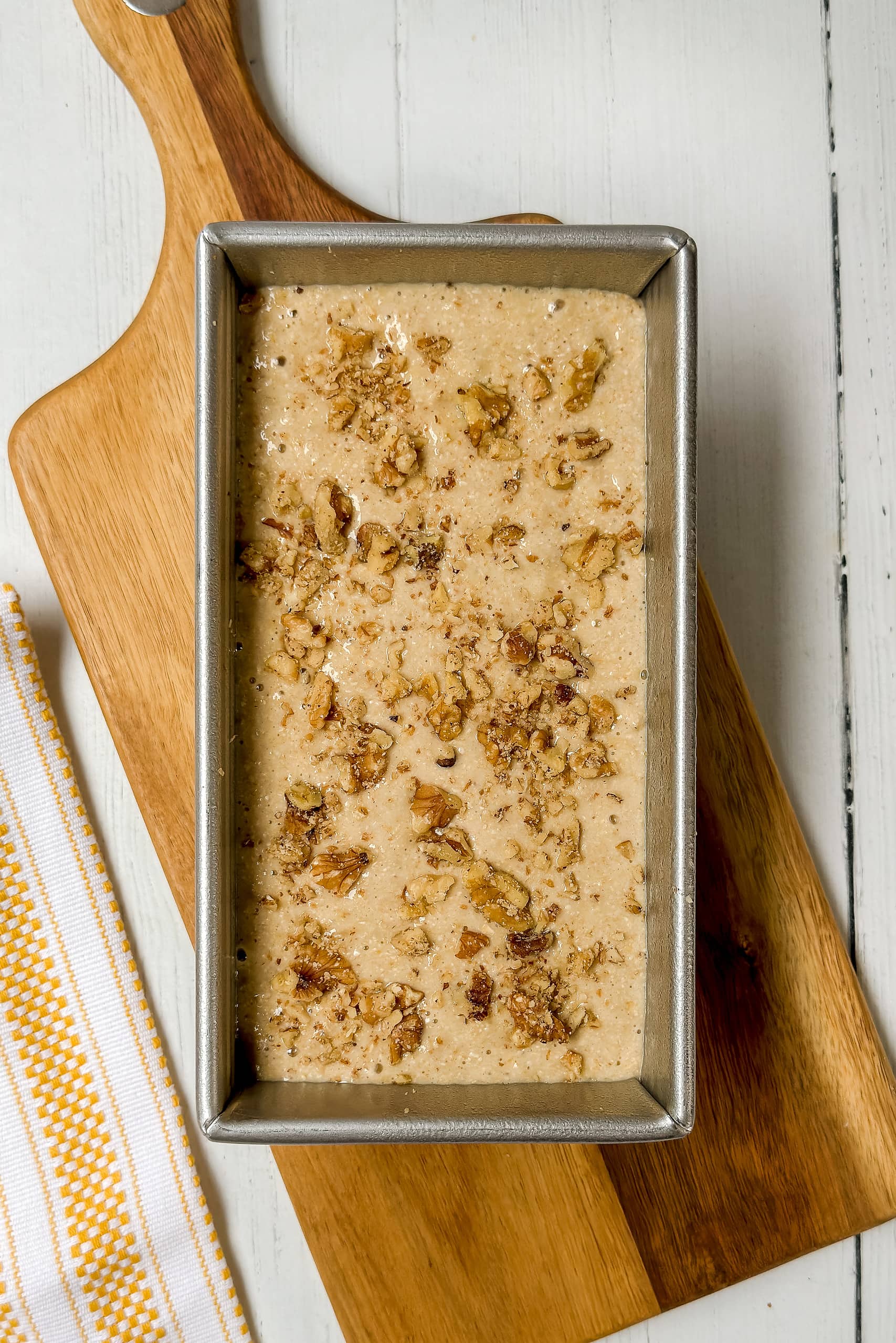 Top view of unbaked Oat Flour Banana Bread sprinkled with chopped walnuts in a metal loaf pan.