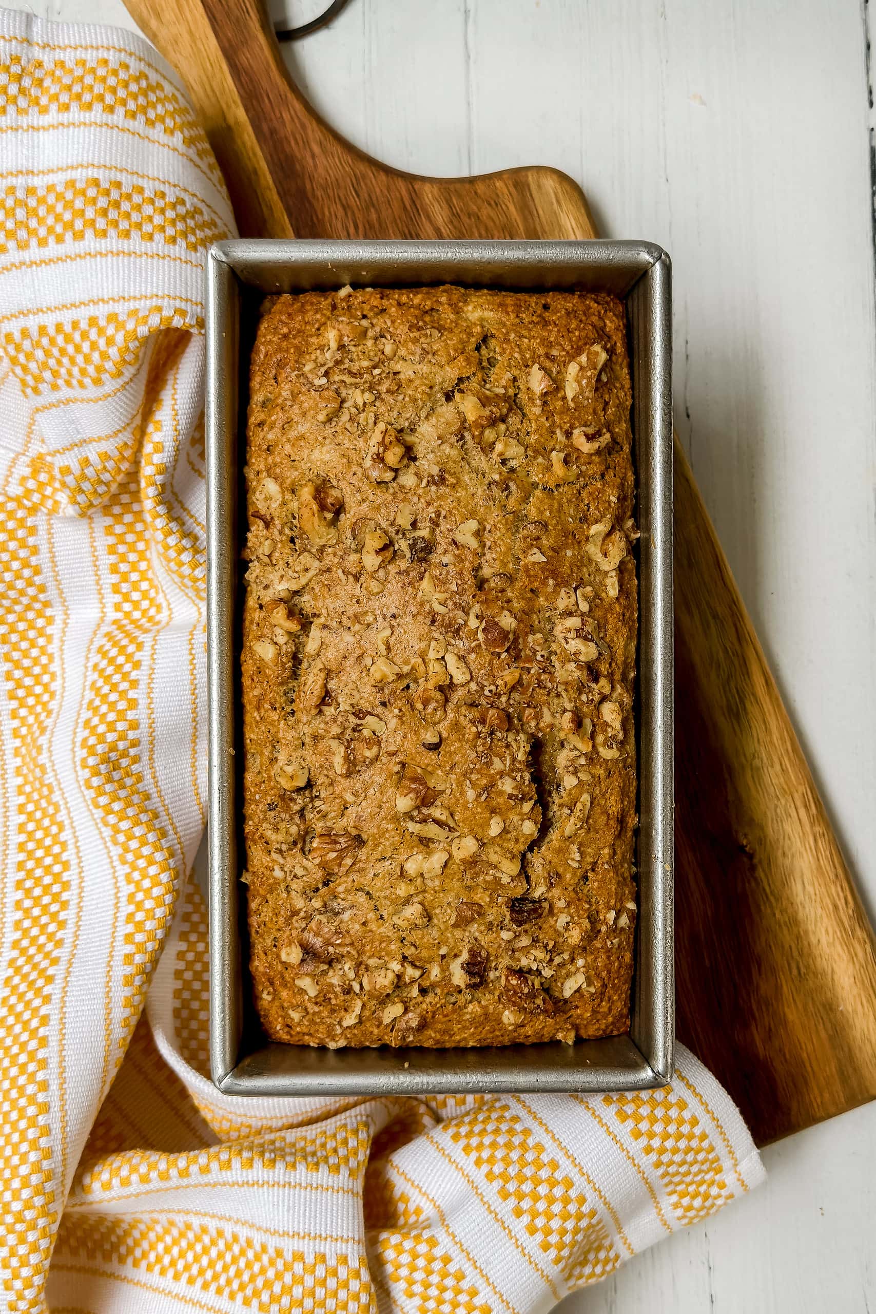Top view of just baked Oat Flour Banana Bread sprinkled with chopped walnuts in a metal loaf pan.