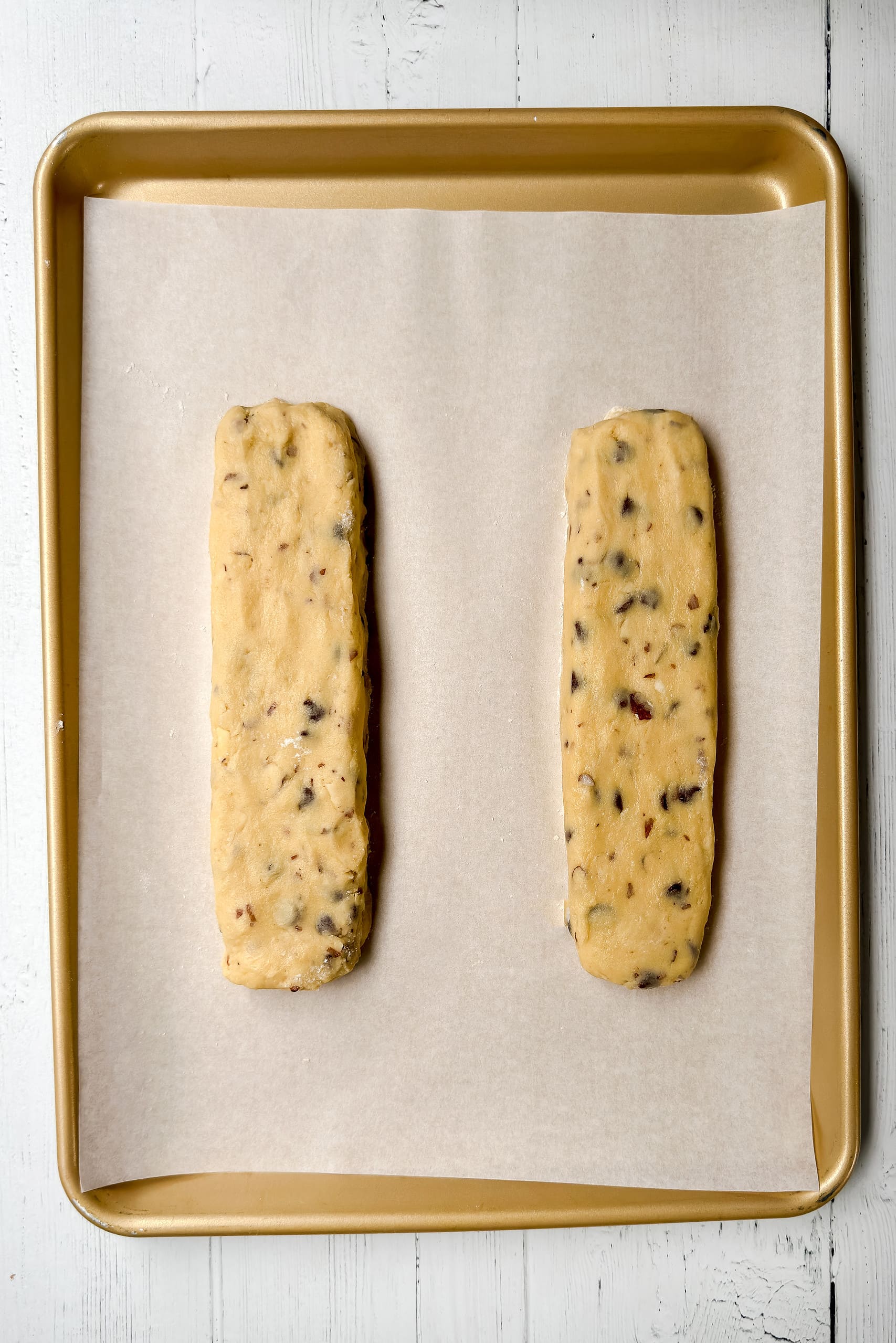 Top vertical view of unbaked biscotti logs on a parchment lined baking sheet.