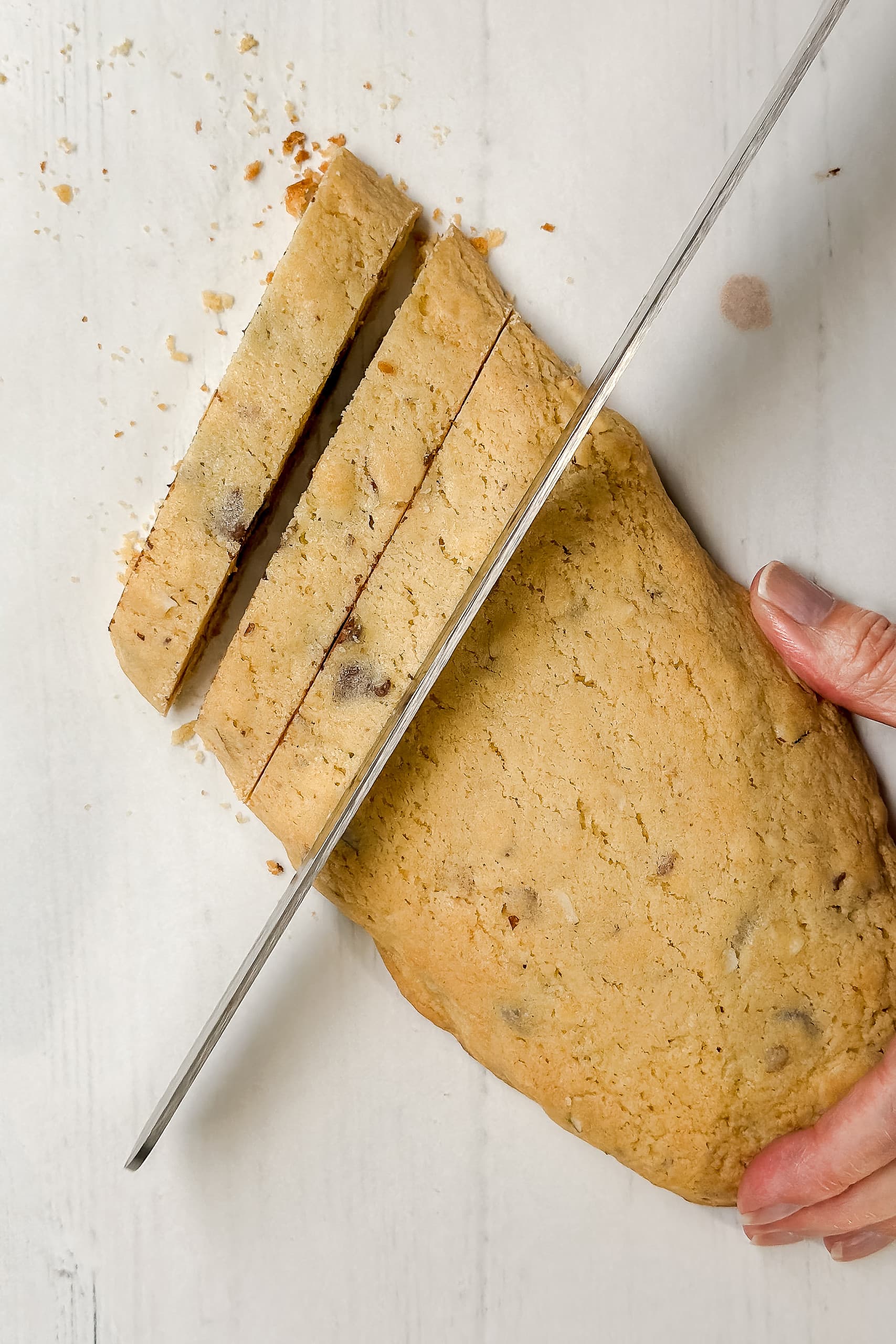 Top vertical view of biscotti log being sliced into cookies using a serrated knife.