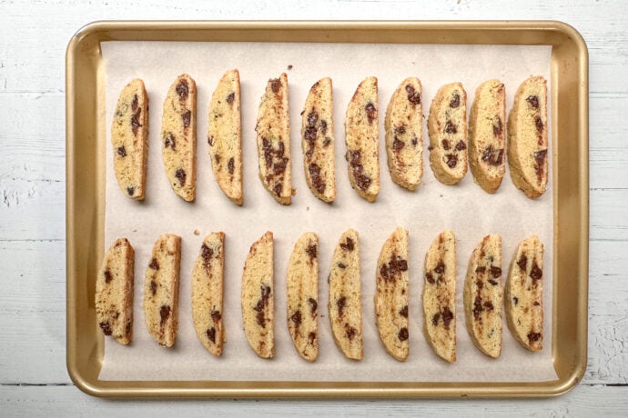 Top view of slices of biscotti on a parchment lined gold baking sheet.