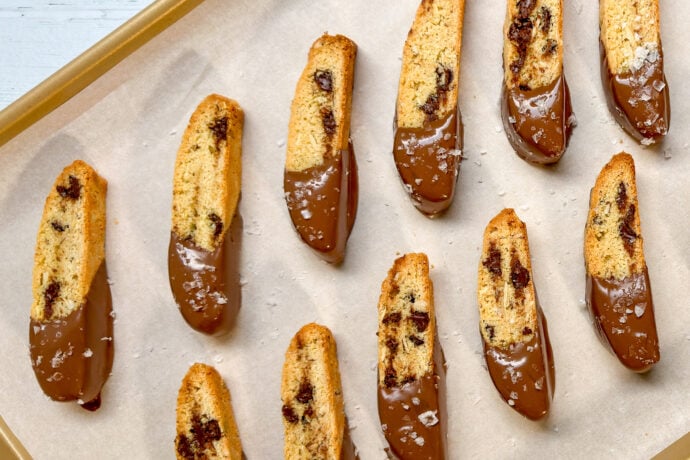 Top view of twice baked biscotti on a parchment lined baking sheet and dipped in chocolate sauce.