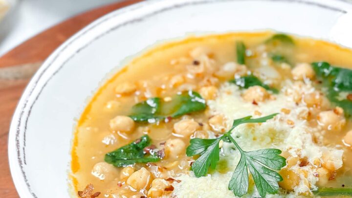 Side view of a white bowl of Curry Chickpea Soup garnished with fresh parsley and Parmesan cheese.