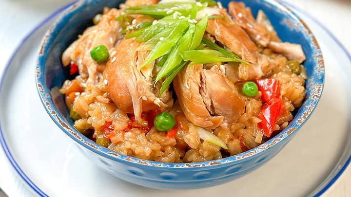 Three-quarters view of Instant Pot Teriyaki Chicken and Rice in a blue bowl with soy sauce and chopped green onions.