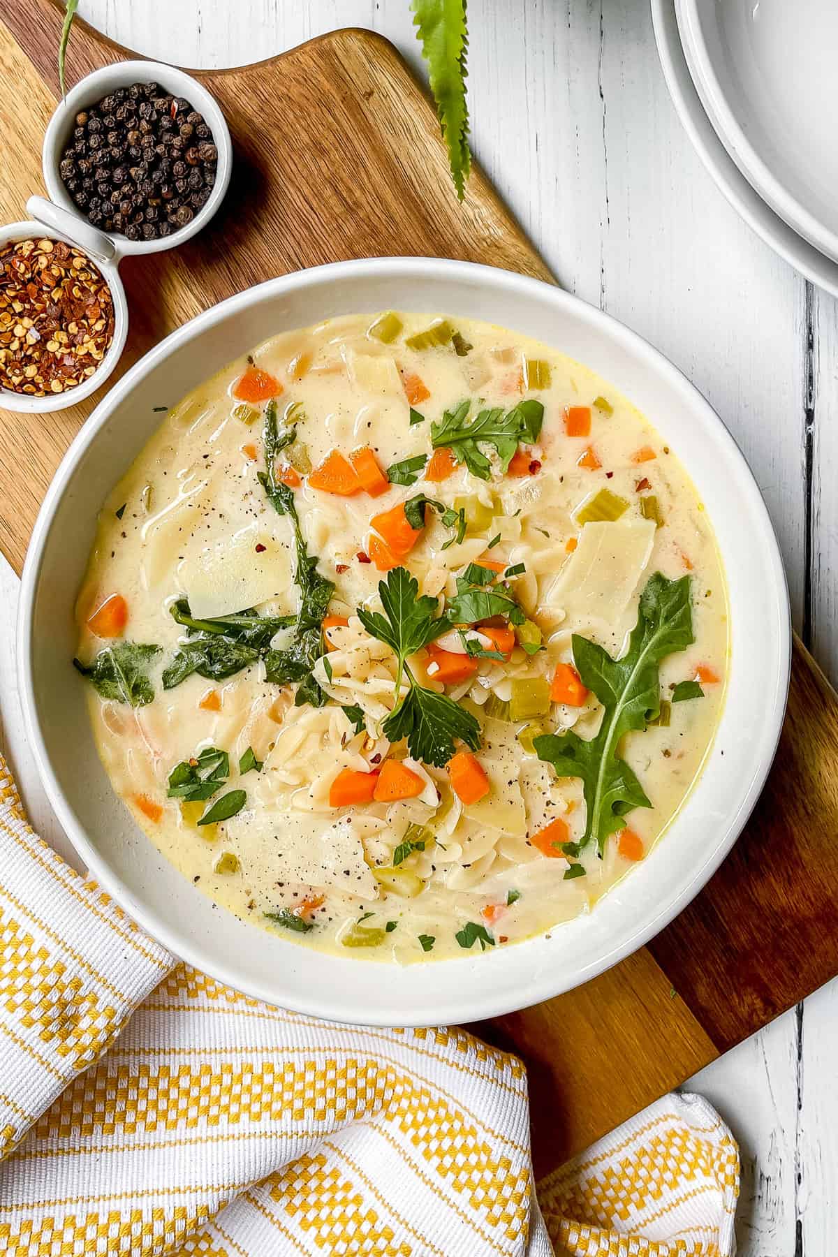 Lemon Chicken Orzo Soup in a white bowl and topped with arugula leaves as garnish and red pepper flakes.
