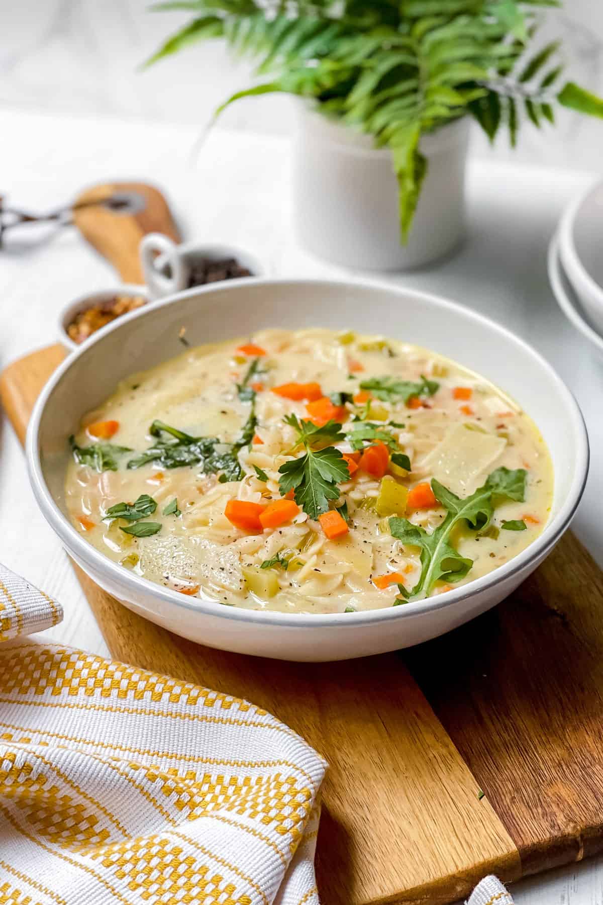 Side view of a white shallow bowl filled with Lemon Chicken Orzo Soup on a wooden serving platter.