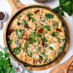 Creamy gnocchi with spinach, sun-dried tomatoes, and herbs served in a skillet on a wooden board—this irresistible gnocchi recipe is surrounded by fresh greens and seasoning bowls.