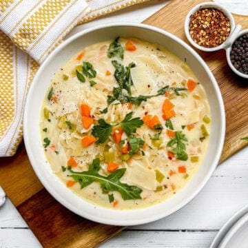 Bowl of Lemon Chicken Orzo Soup is garnished with fresh arugula leaves and red pepper flakes.
