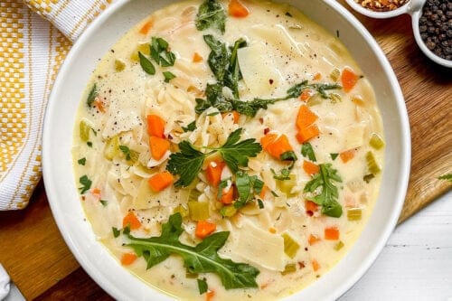 Bowl of Lemon Chicken Orzo Soup is garnished with fresh arugula leaves and red pepper flakes.