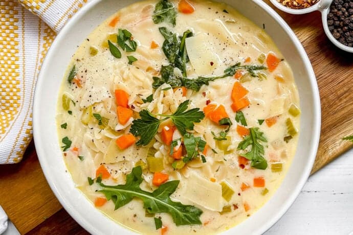 Bowl of Lemon Chicken Orzo Soup is garnished with fresh arugula leaves and red pepper flakes.