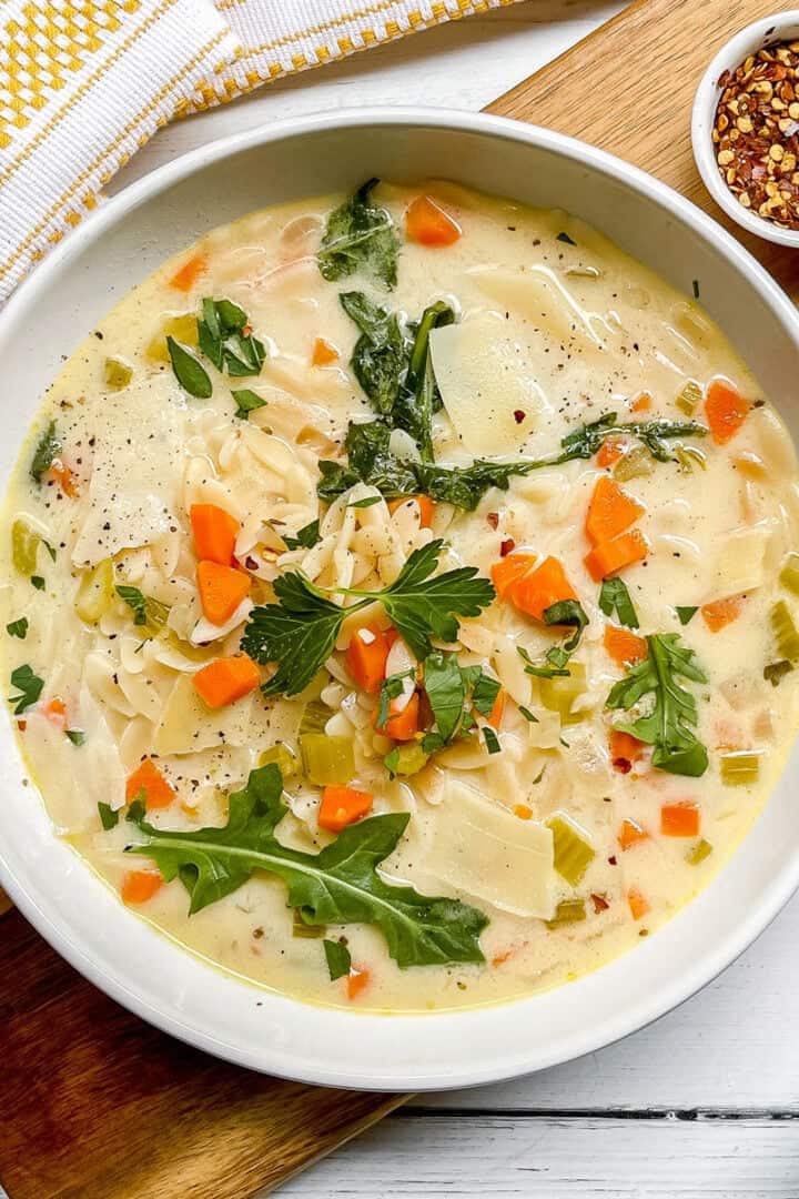 Bowl of Lemon Chicken Orzo Soup is garnished with fresh arugula leaves and red pepper flakes.