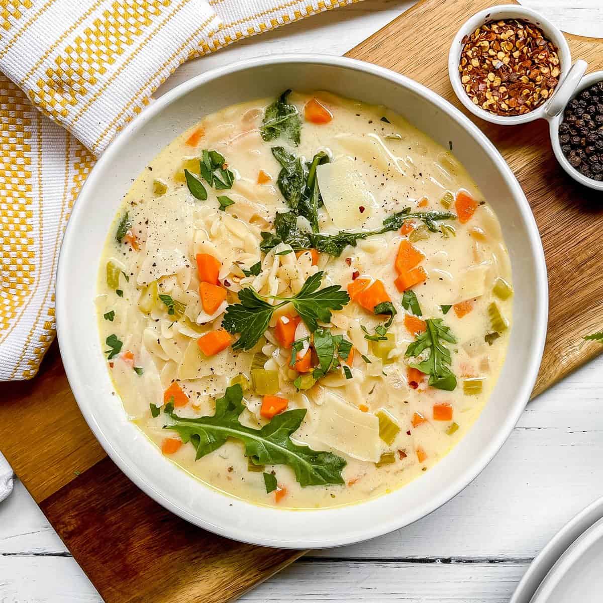 Bowl of Lemon Chicken Orzo Soup is garnished with fresh arugula leaves and red pepper flakes.