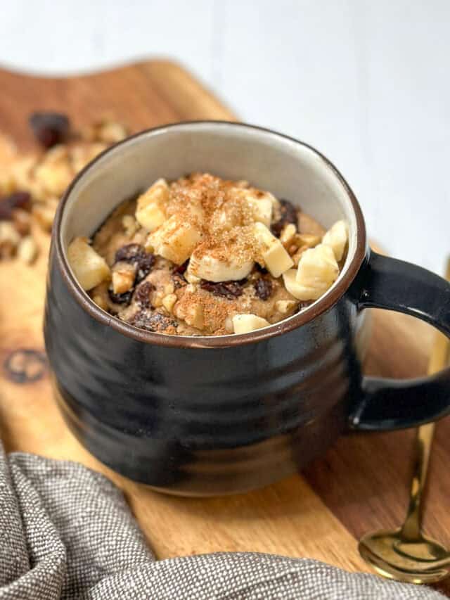 Side three-quarter view of ready to eat 2 Minute Banana Bread Mug Cake with chopped bananas, raisins, walnuts, and a sprinkling of brown sugar.