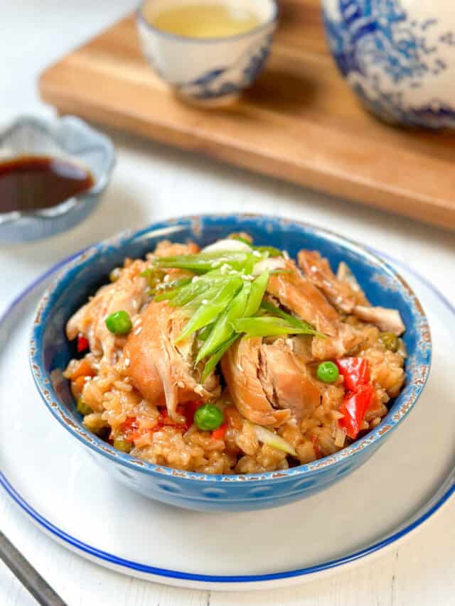 Three-quarters view of Instant Pot Teriyaki Chicken and Rice in a blue bowl with soy sauce and chopped green onions.