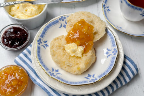 Horizontal side view of drop biscuit on a white and white plate with melting butter and marmalade jam.