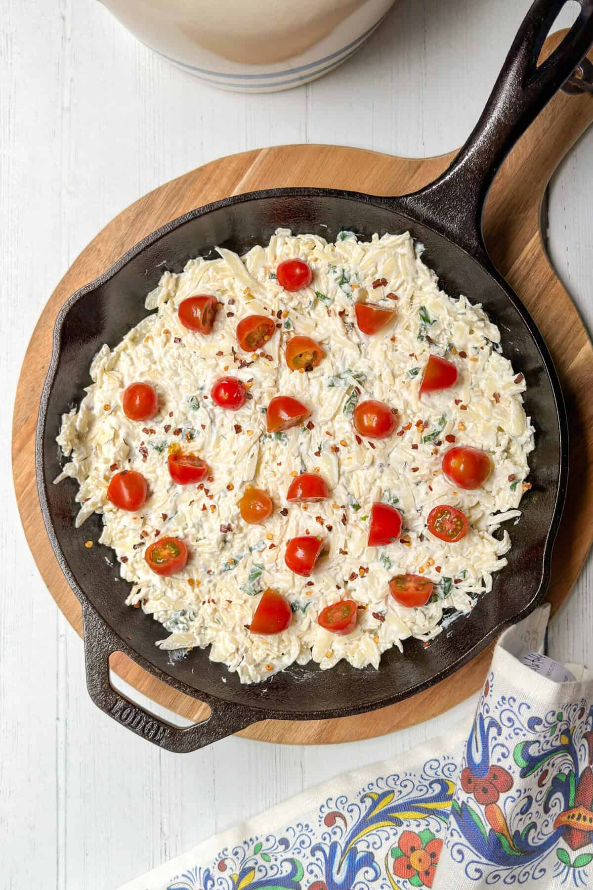 Top view of unbaked Hot Caprese Dip with halved cherry tomatoes in a cast iron skillet.