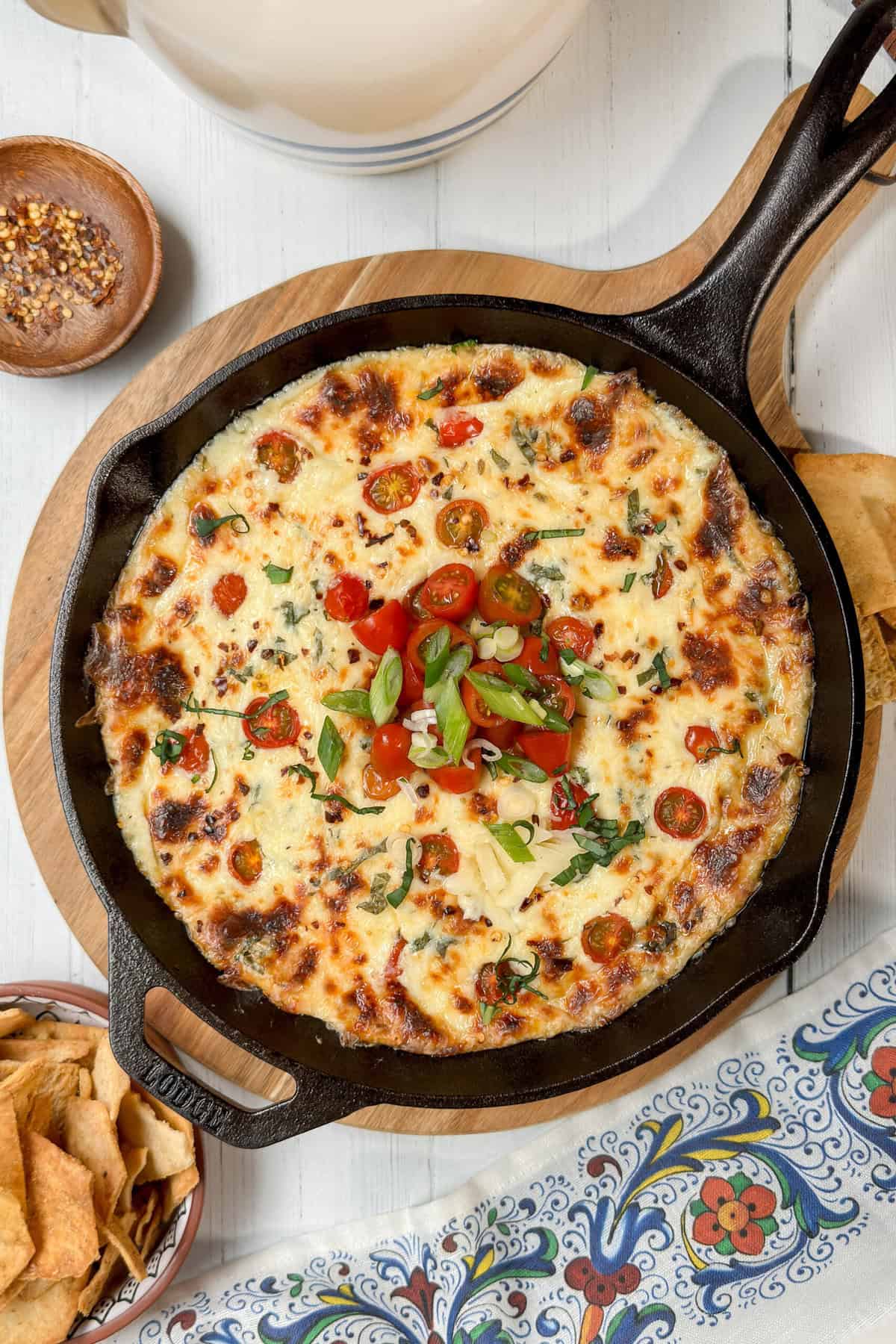 Top view of baked Hot Caprese Dip in a cast iron skillet with fresh green onions and cherry tomatoes as garnish.