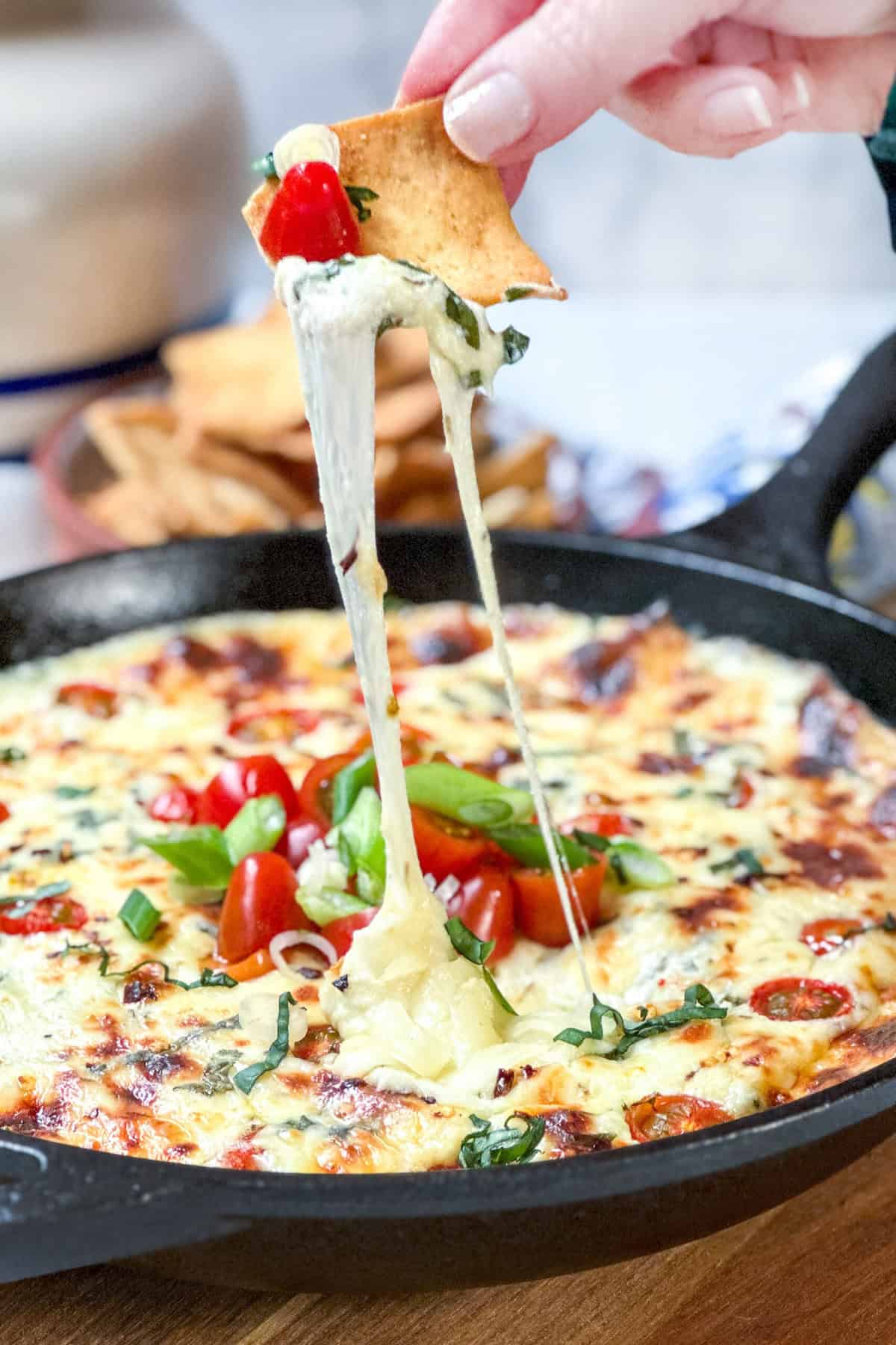 Side view of Hot Caprese Dip with pitas and cheese pulling up from the dish.