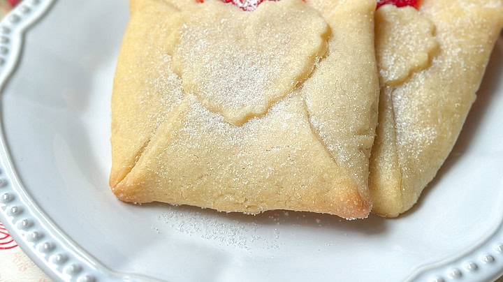 Closeup view of Love Letter Butter Cookies on a white plate with strawberry jam filling.