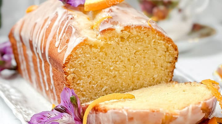 Front side view of sliced Orange Cake with citrus icing and orange slices on a white serving platter.